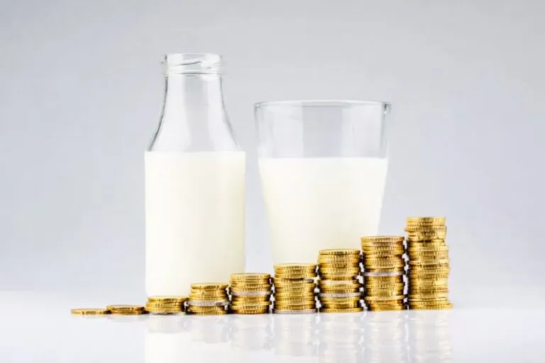 Botella y vaso con leche acompañados de pilas de monedas, ilustrando el aumento de precios por inflación