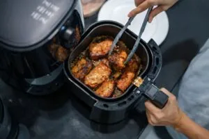 Persona cocinando con una air fryer moderna y mostrando alimentos dorados crujientes y técnicas correctas de uso.