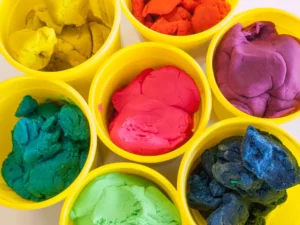 Botes de Play-Doh de colores utilizados por niños para crear figuras y desarrollar su creatividad.