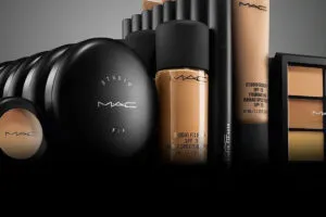 Productos icónicos de MAC Cosmetics en un mostrador de maquillaje con labiales, brochas y empaques negros característicos de la marca.